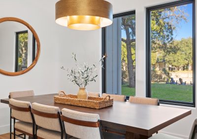 Dining area with brass chandelier, dark wood table, and windows overlooking a large lawn and Lake LBJ channel.