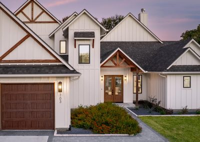Modern farmhouse exterior with board-and-batten siding, wood garage doors, and exposed gable trusses over the entry.