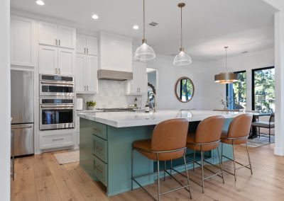 Kitchen with sage green island, white cabinetry, pendant lights, waterfall countertop, and leather bar seating.