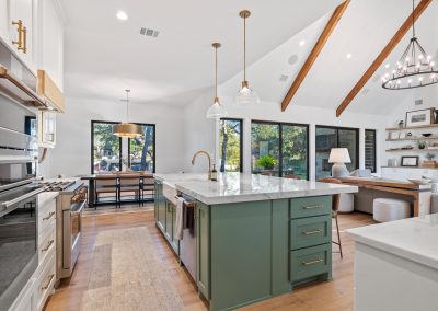 Open-concept kitchen with sage green island, marble countertops, vaulted ceilings, and brass lighting fixtures.