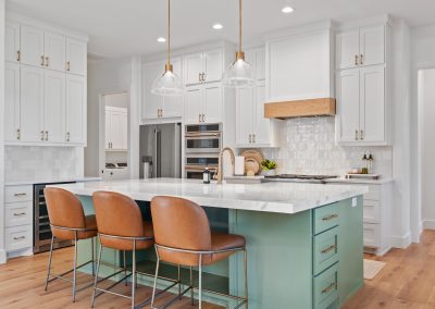 Kitchen with sage green island, marble countertops, leather bar stools, built-in wine cooler, and wood range hood.
