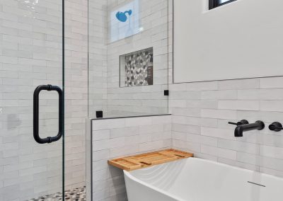 Modern bathroom with frameless shower, soaking tub, pebble tile floor, subway tile walls, and matte black fixtures.