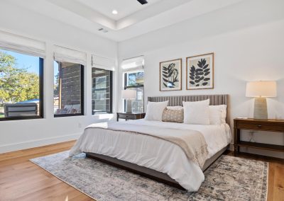 Primary bedroom with tray ceiling, large windows, natural light, white walls, and hardwood floors in a modern farmhouse design.