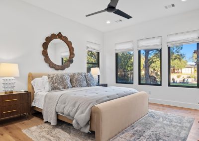Bedroom with large windows, natural light, upholstered bed, hardwood floors, and white walls in a modern farmhouse design.