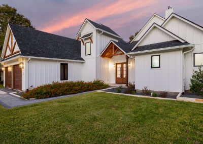Side view of modern farmhouse with board-and-batten siding, wood accents, gabled rooflines, and covered entry.