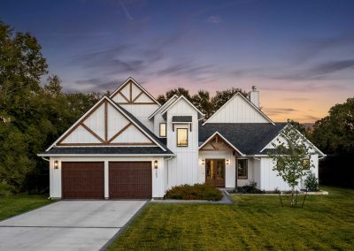Twilight view of modern farmhouse exterior with white board-and-batten siding, wood gable accents, and double garage.