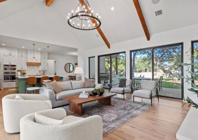 Open living space with vaulted ceilings, large windows, sage green island, pendant lighting, and wide-plank hardwood flooring.