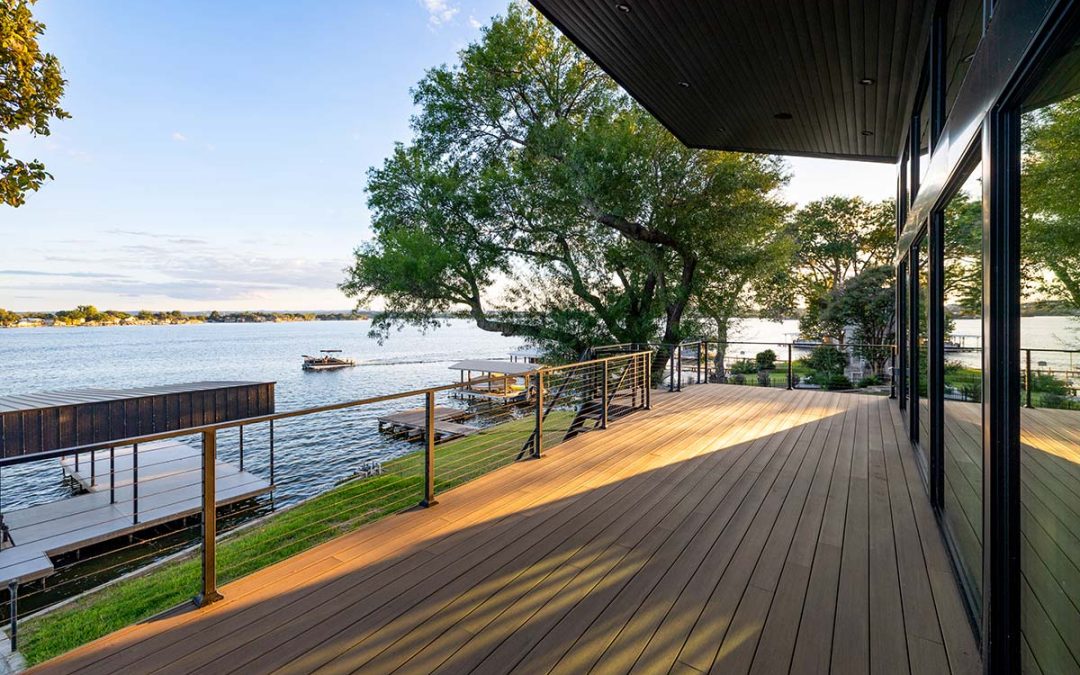 Outdoor living features for lake homes including a covered deck with expansive glass walls, cable railing, and direct views of Lake LBJ shoreline.